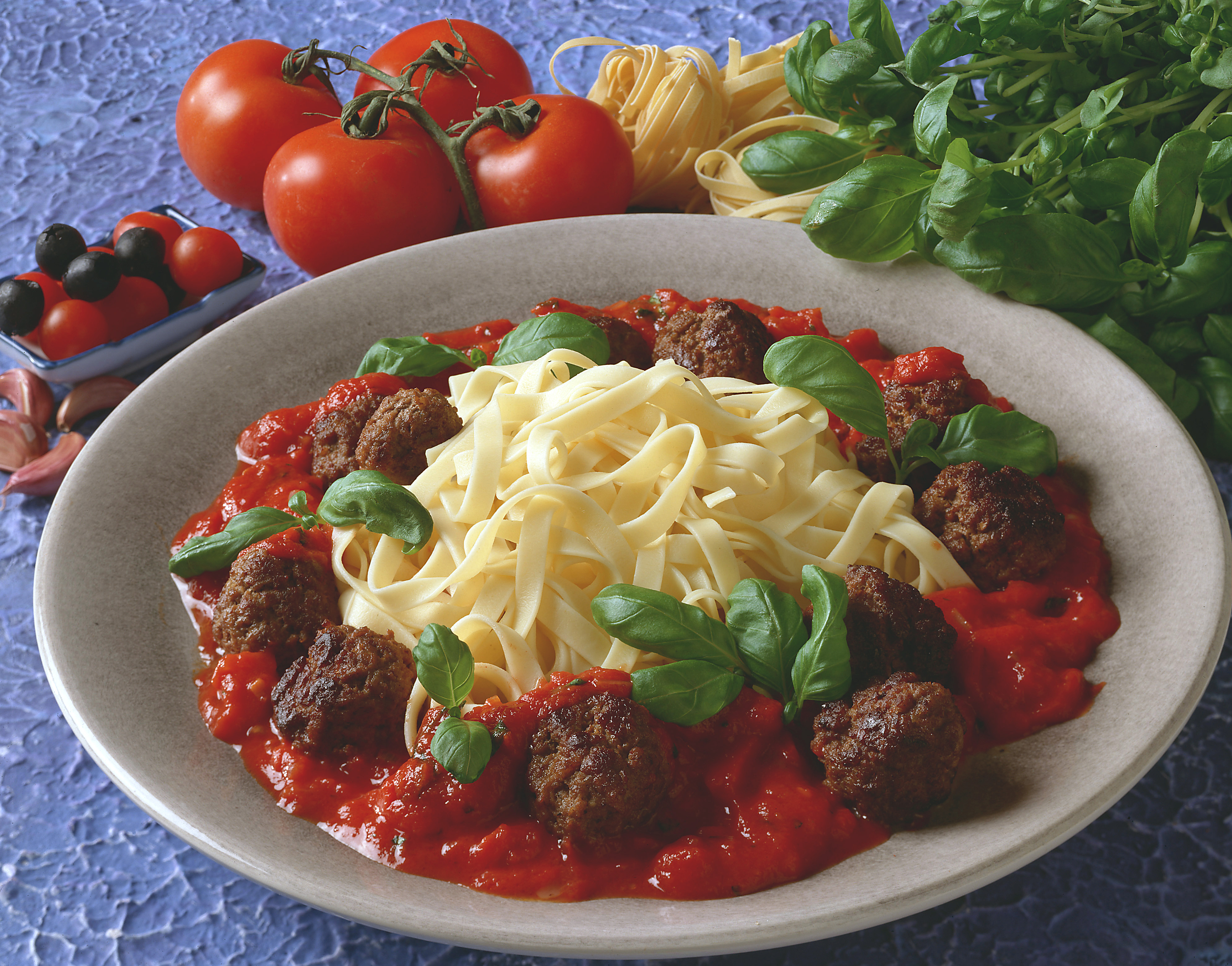 Kjøttboller i tomatsaus med pasta på en hvit tallerken. Foto.