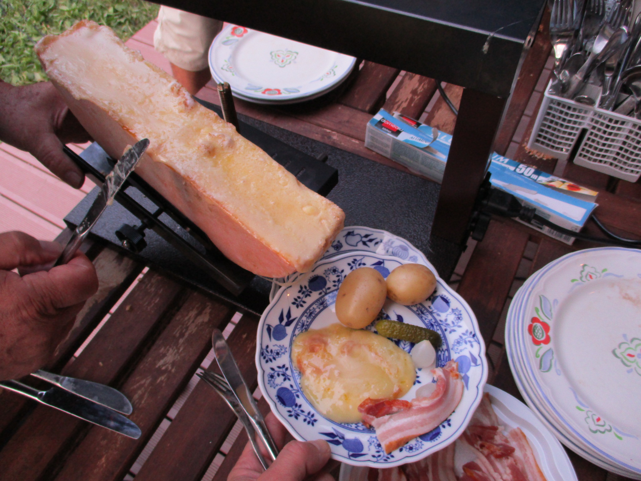 Et raclette-måtid. Smeltet ost skrapes av på en tallerken og serveres med potet, sylteagurk, sølvløk og bacon. Foto.