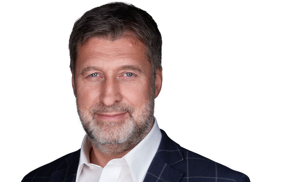 Mann med kort skjegg, blå jakke og hvit skjorte. Foto.