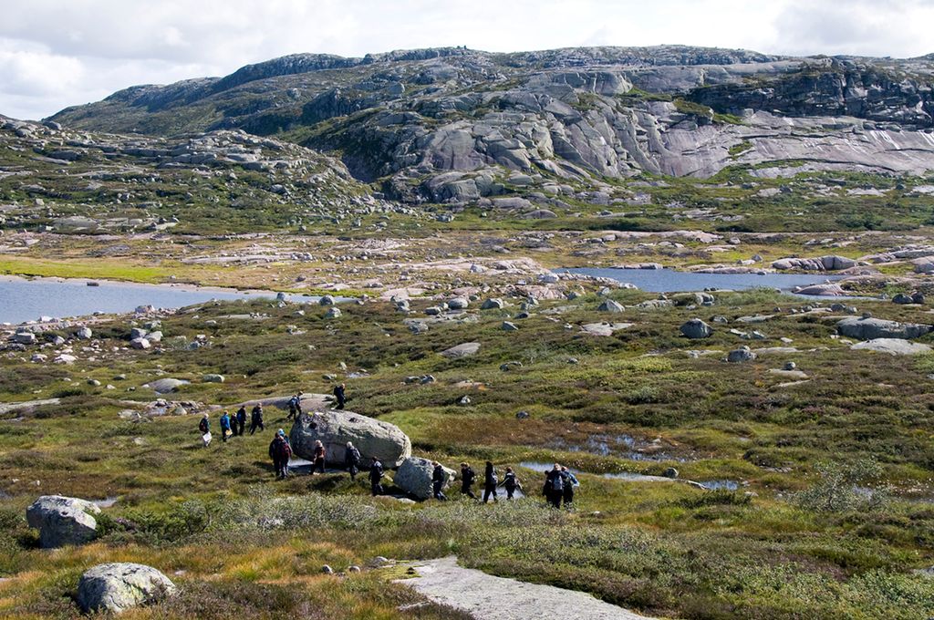 En gruppe folk ferdes i et fjellandskap med noe vegetasjonsdekke. Foto.