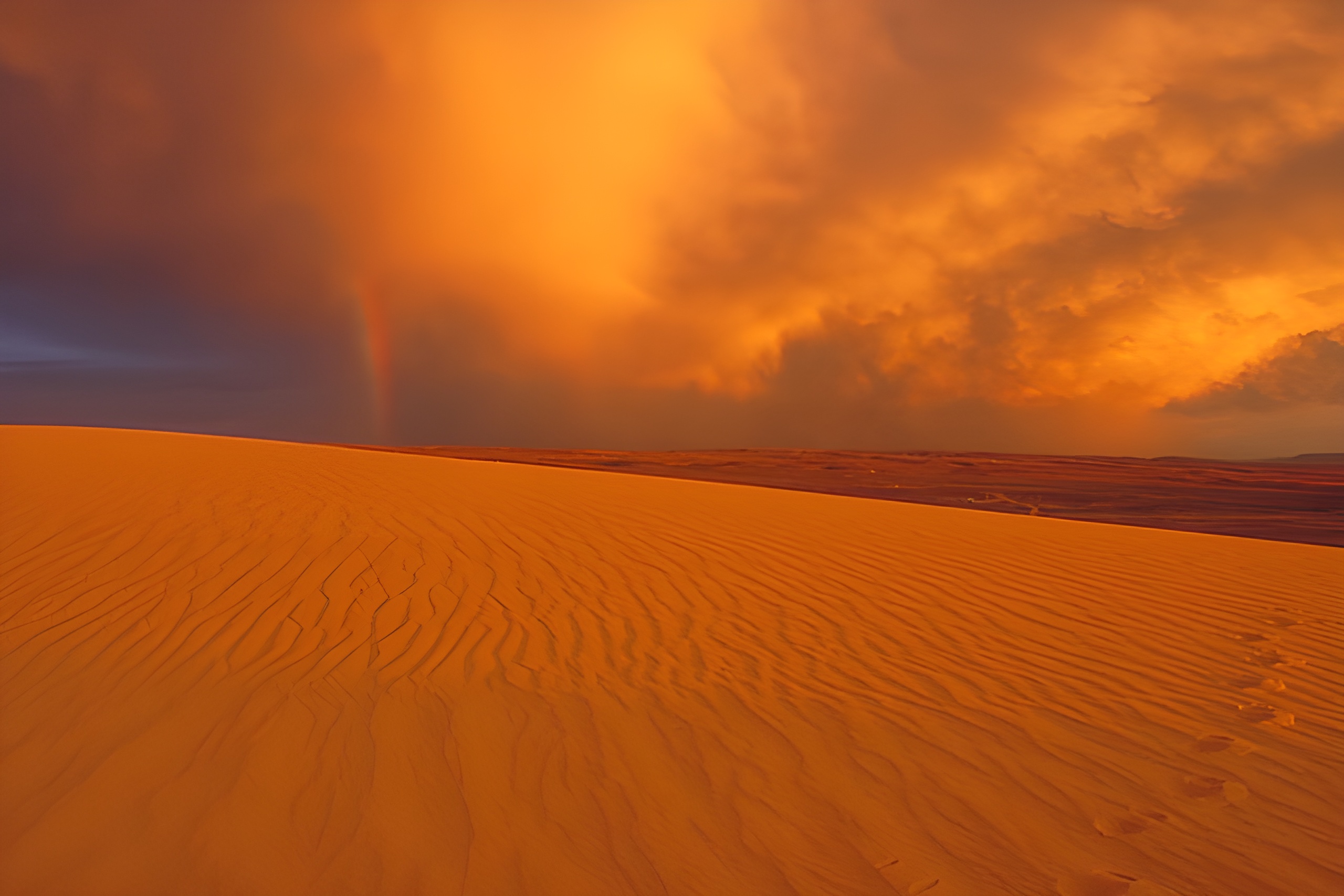 Ørkenlandskap i oransje og brune toner med en gyllen himmel over. Foto.