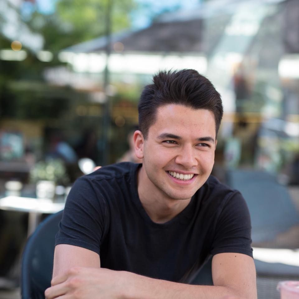 Ung mann sitter smilende med armene i kors. Foto.