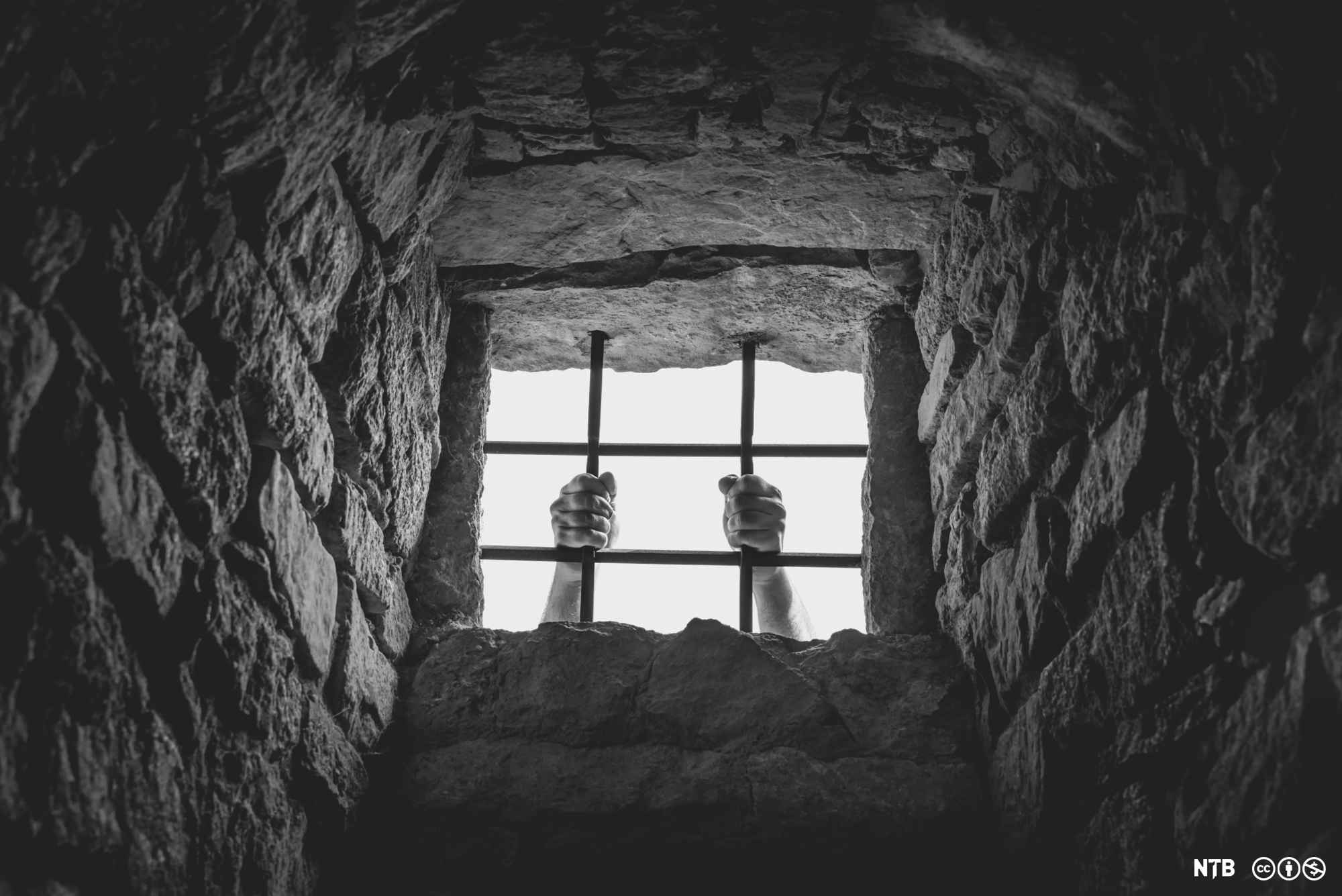 A man is holding on to the bars in a prison window.  