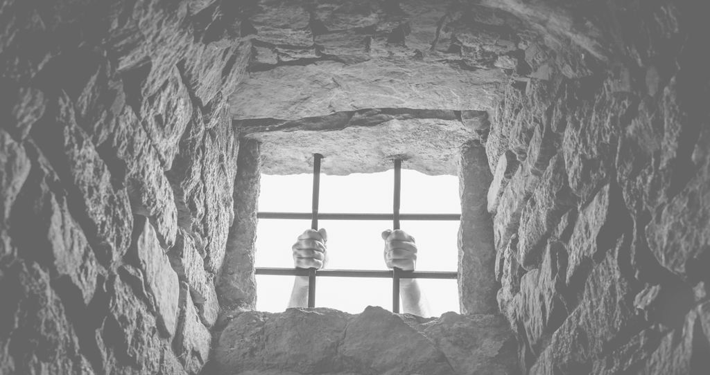 A man is holding on to the bars in a prison window.
