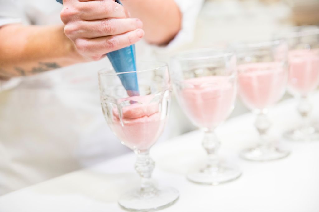 En konditor sprøyter bærmousse fra en sprøytepose over i glass. Foto.