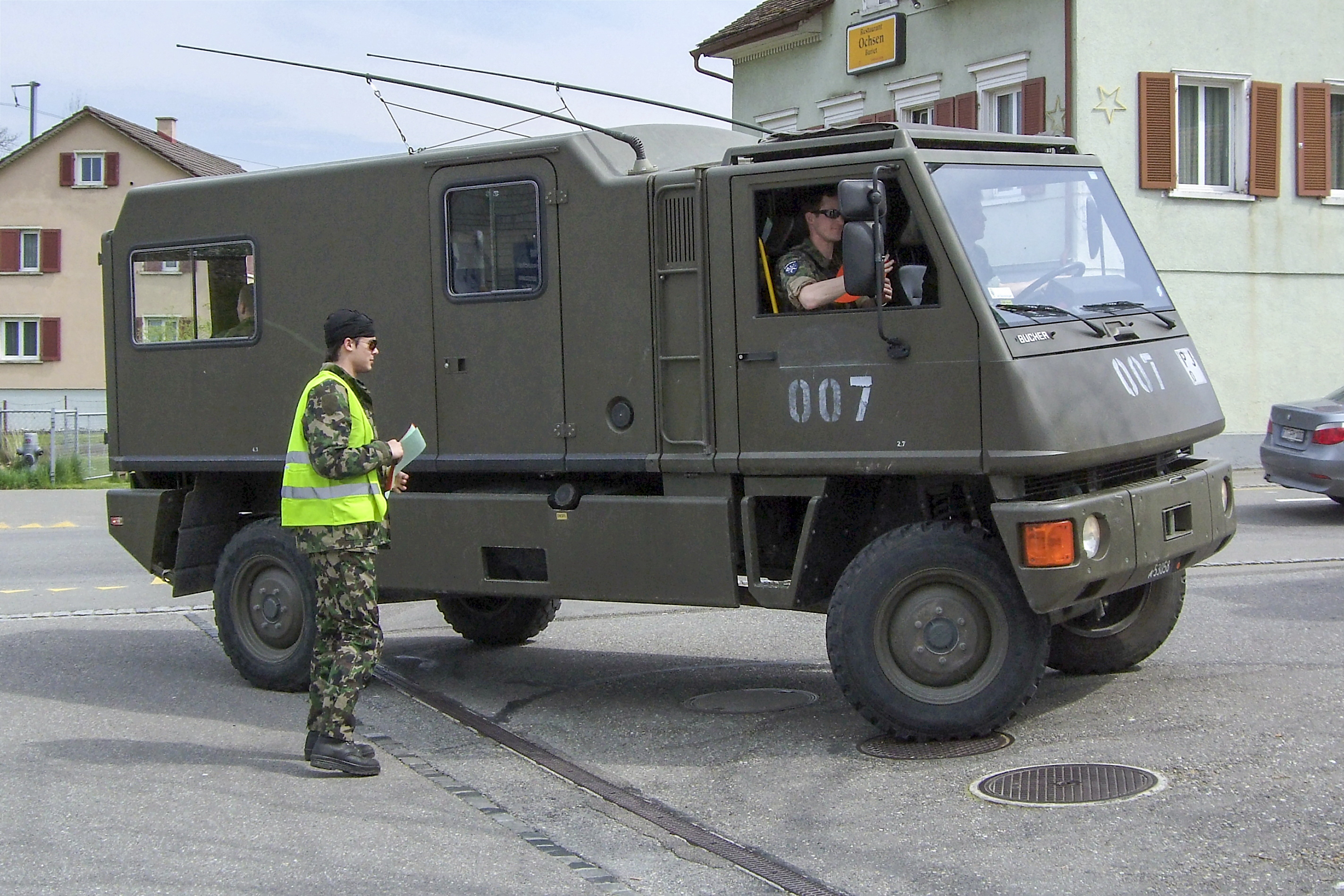 Ung soldat i uniform og refleksvest står foran et militært kjøretøy. Foto.