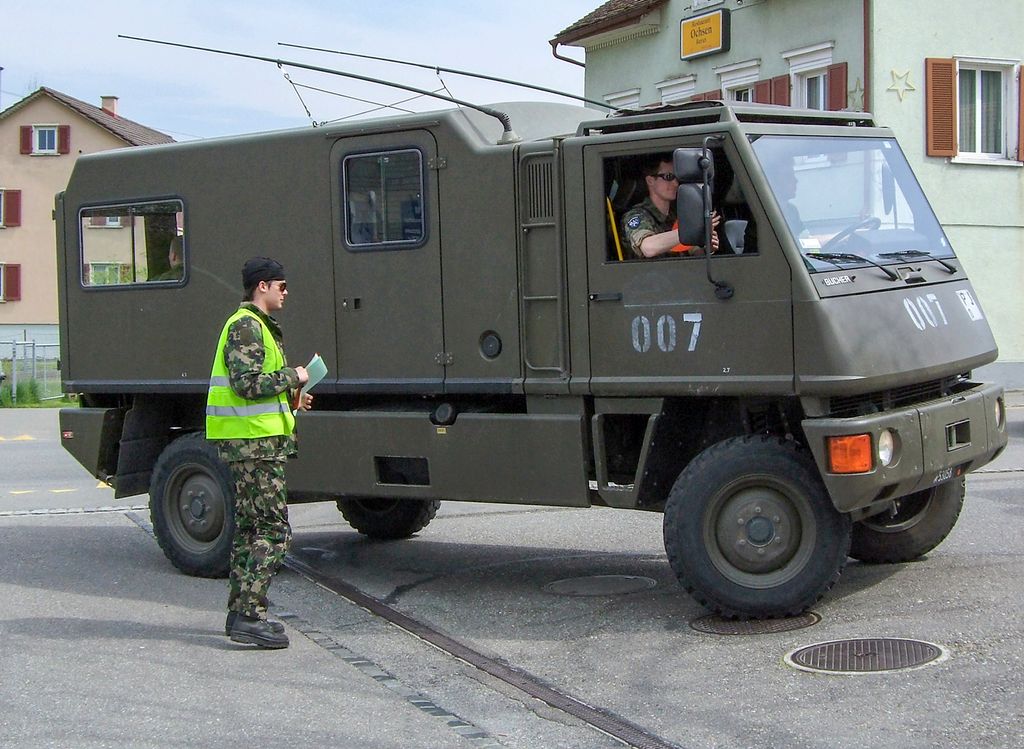 Ung soldat i uniform og refleksvest står foran et militært kjøretøy. Foto.