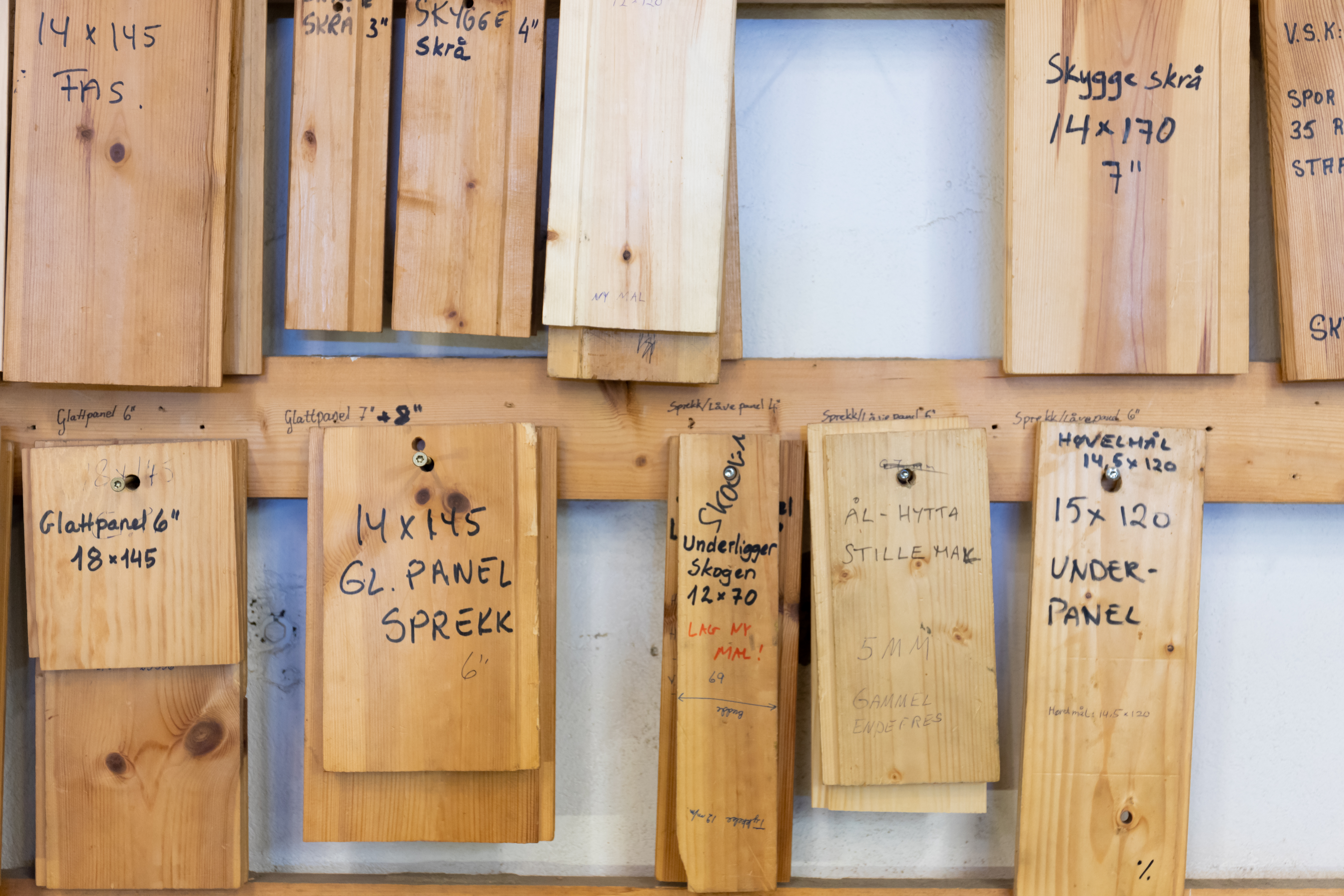 Små biter av ulike typer panel som henger på lister på veggen. Bitene er påskrevet paneltype og dimensjon. Foto.