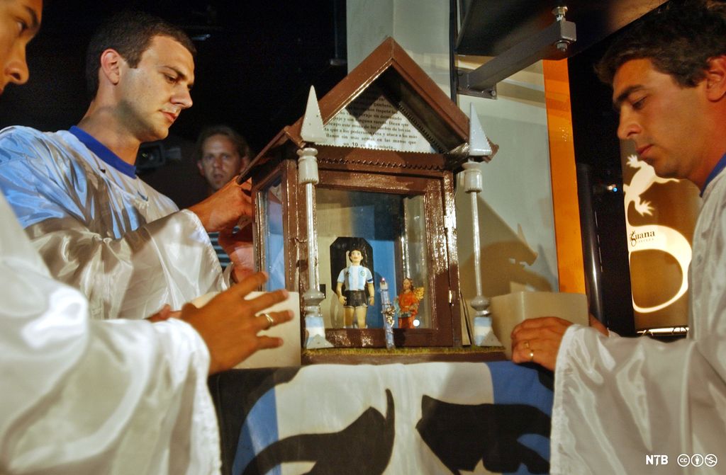 Menn i hvite kjortler med en julekrybbe der det er plassert en figur av en fotballspiller i Argentinas landslagsdrakt sammen med en knelende engel. Foto.