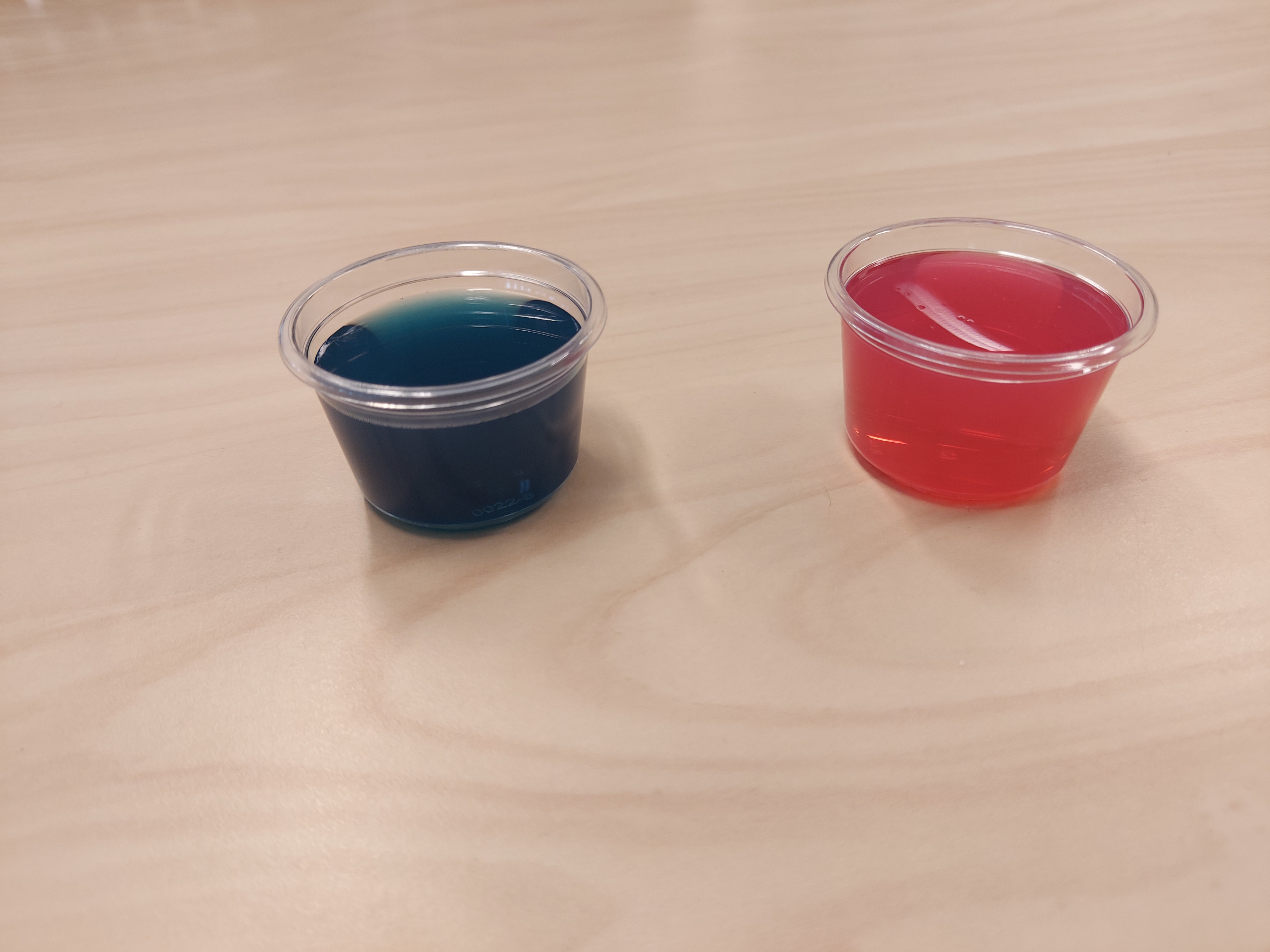 To plastkopper. Det er blå væske i den ene og rødrosa væske i den andre. Foto.