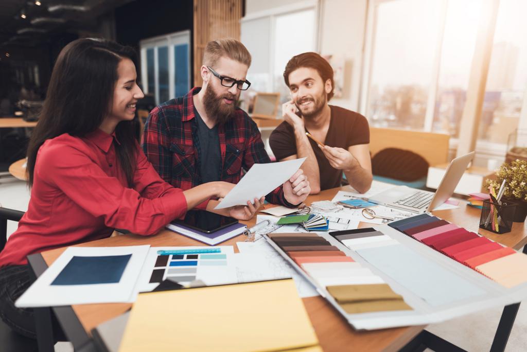 Tre designarar diskuterer fargeval og skisser. Foto.