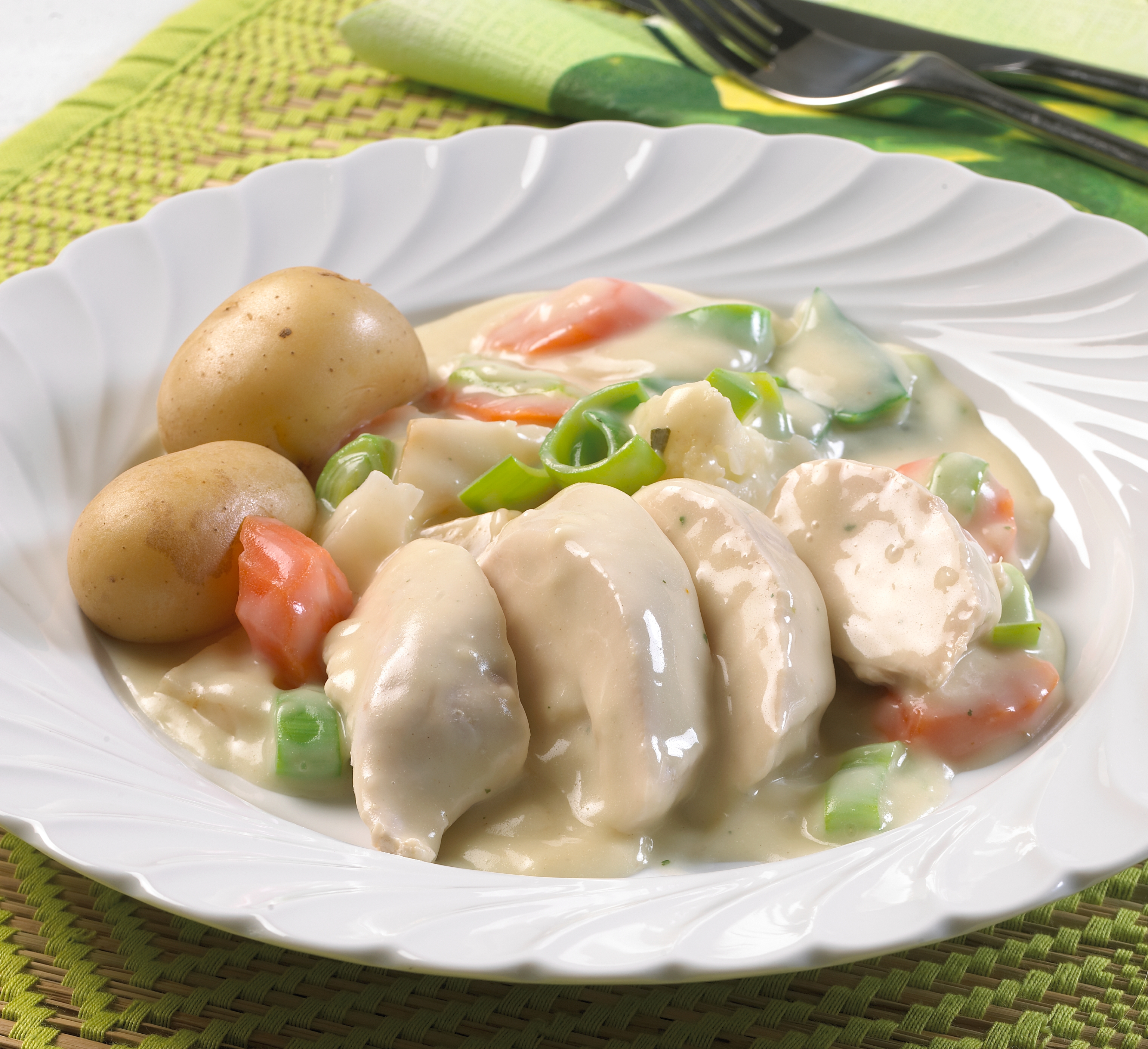 Tallerken med kyllingbitar, grønsaker og potetar med lys saus. Foto.