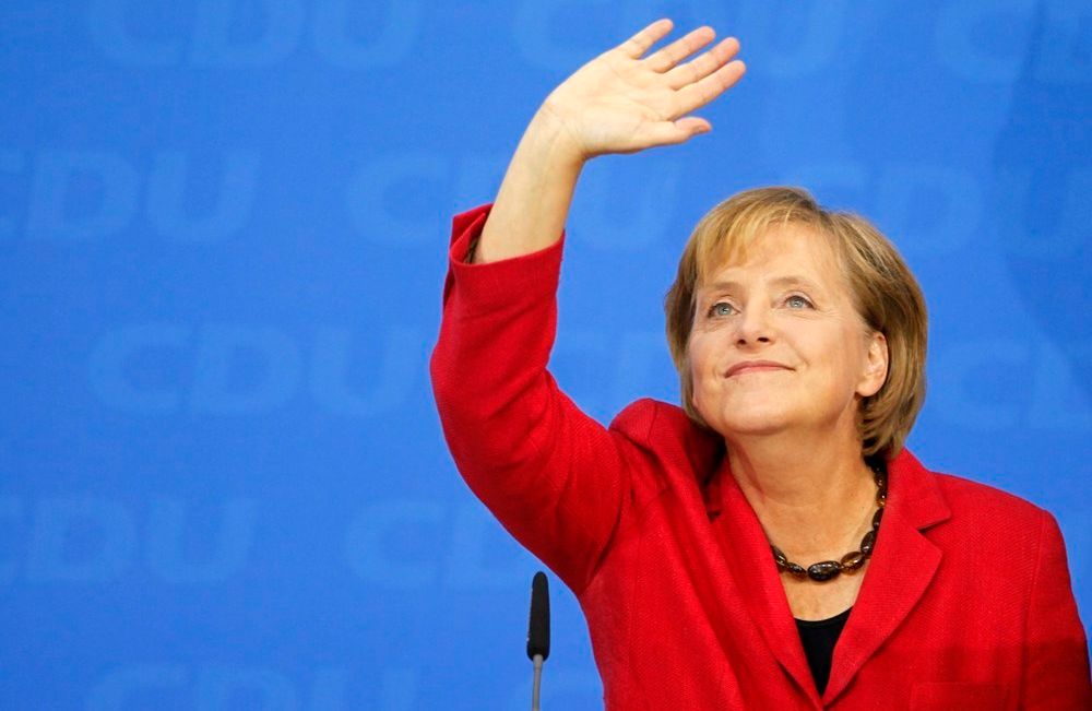 Den tyske politikeren Angela Merkel på et partimøte. Hun har på seg en rød blazer over en svart genser og et halskjede satt sammen av store, mørke, avlange steiner. Foto.