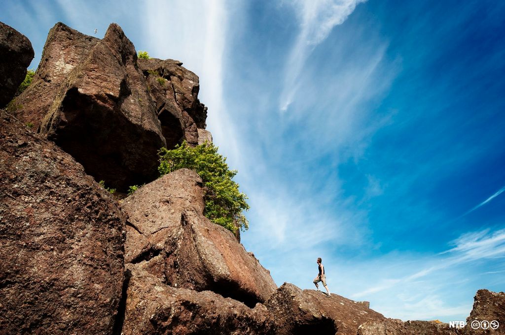 Steep mountain side, man standing at the bottom, blue sky above. Photo.