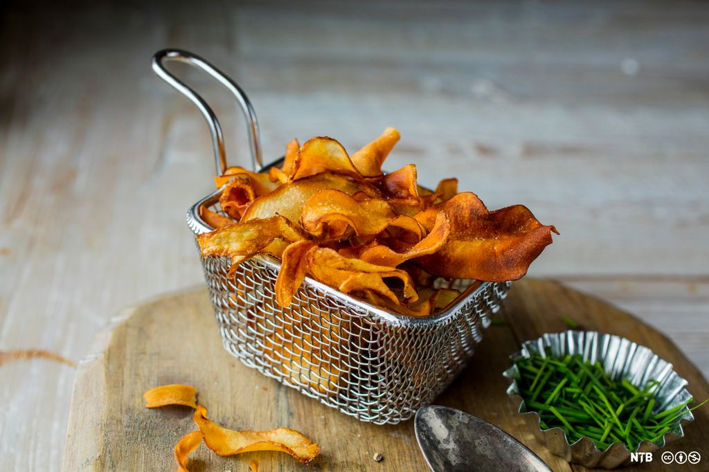 Ferdig fritert jordskokkchips i en frityrkurv som står på ei skjærefjøl. Foto.