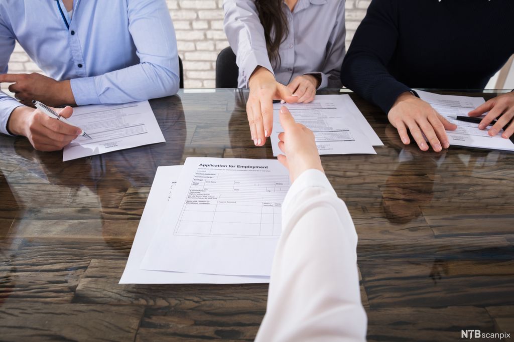 En person rekker hånda fram for å takke for intervjuet. På andre sida av bordet sitter det tre ansatte fra bedriften. Foto.