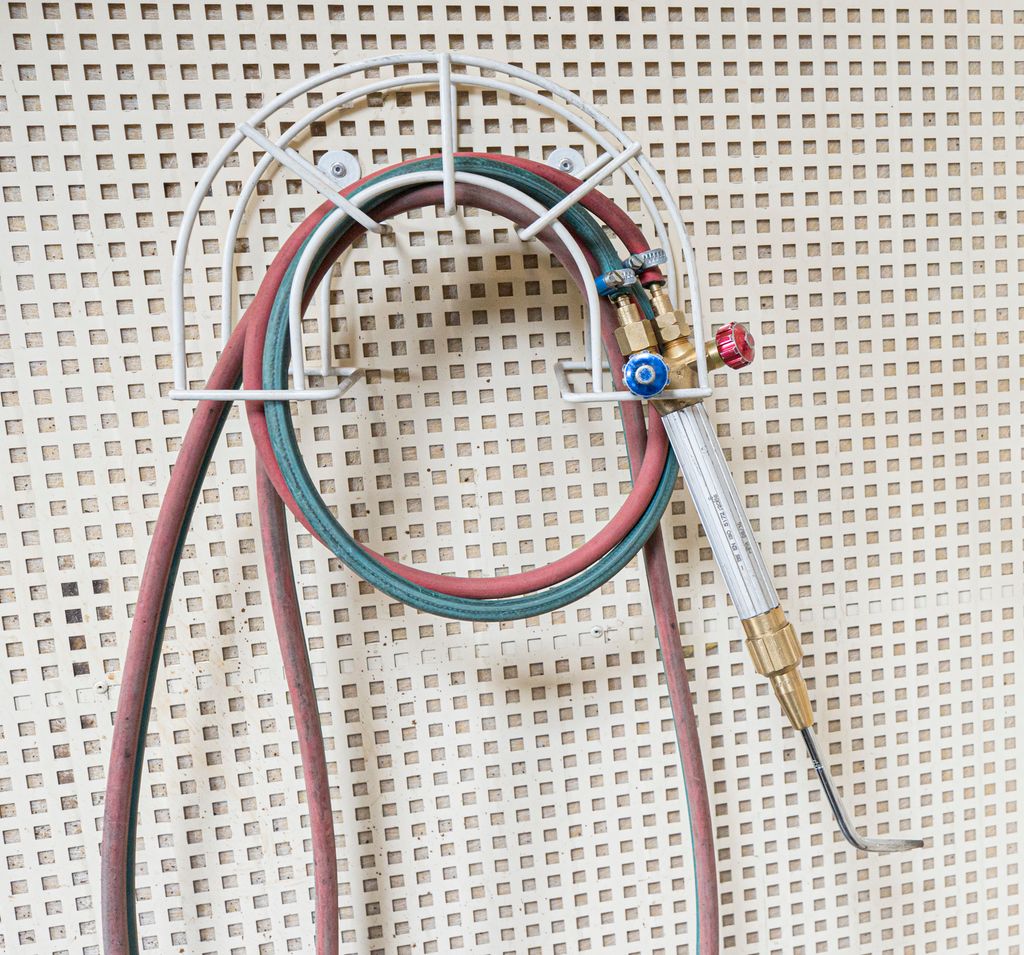 Gassbrennar med slange i ein haldar på veggen. Foto.