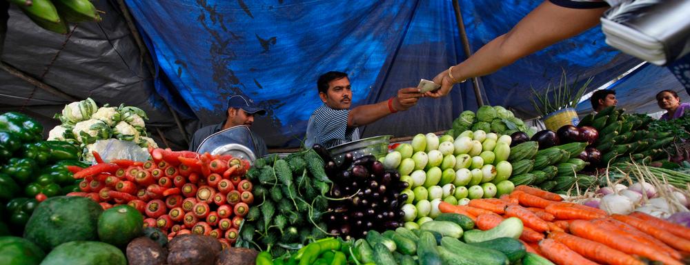 Ein seljar på ein marknad sel grønsaker til ein kjøpar. Foto. 