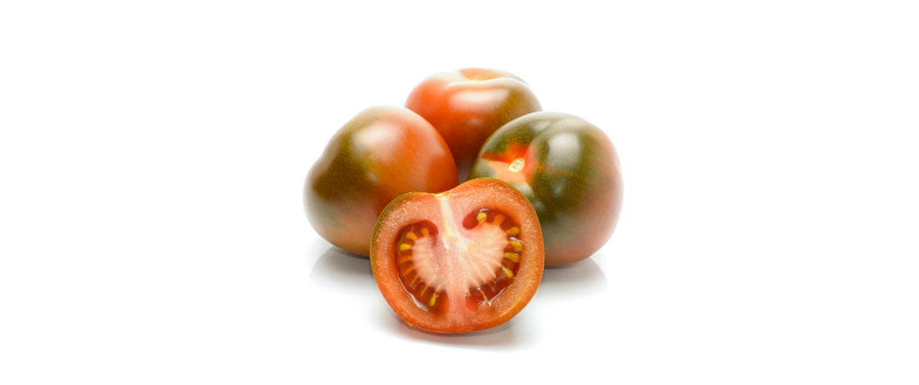Tverrsnitt av rød-grønn tomat. Tre hele tomater ligger i bakgrunnen. Foto.