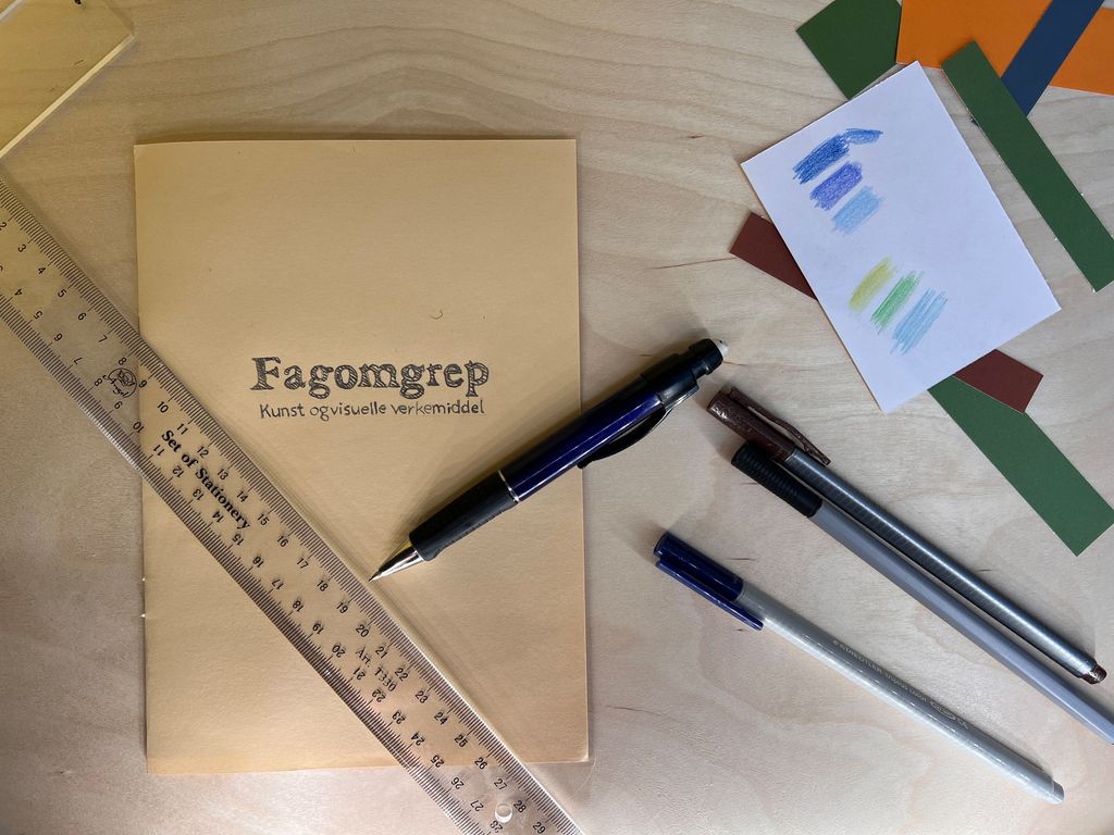 Tittelsida til omgrepsheftet og teiknesaker på arbeidsbordet. Foto.