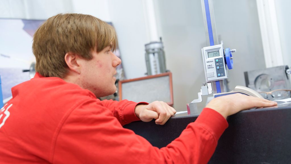 Person står på huk ved et bord og ser på et måleverktøy på bordet. Foto.