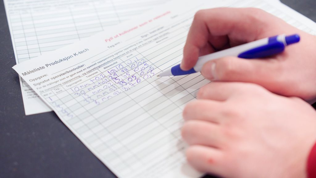 En person skriver tall på et skjema hvor det står Måleliste Produksjon K-tech. Foto.