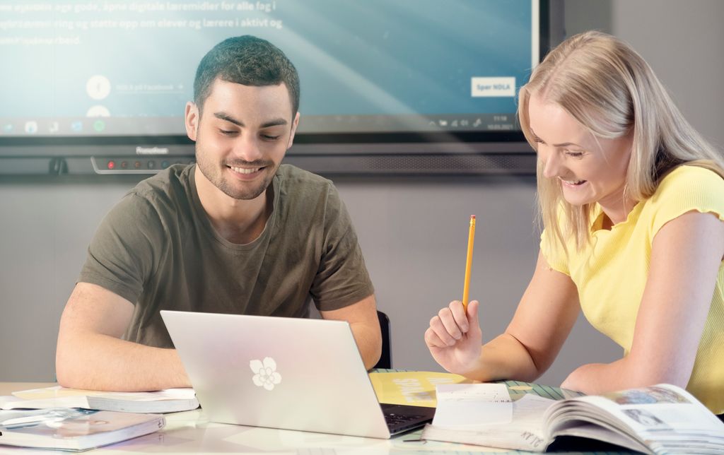 Gutt og jente studerer sammen ved et bord med bærbar datamaskin og bøker. Foto.