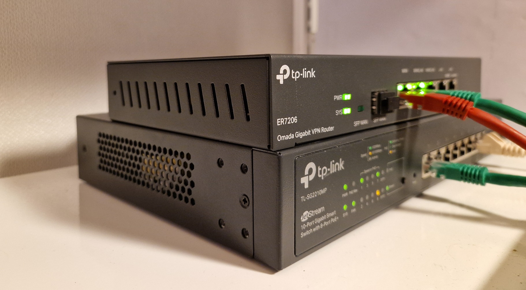 To metallbokser står oppå hverandre på ei hylle, begge har flere lys og nettverksporter på framsiden. Den ene er merket "Router", og den andre er merket "Switch". En kabel går mellom enhetene. Foto.