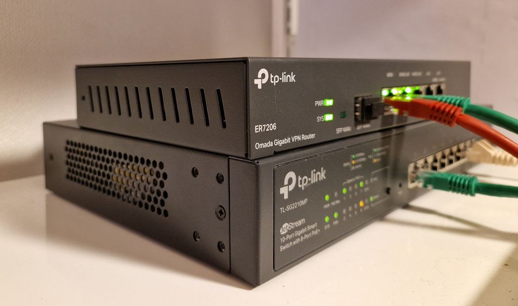 To metallbokser står oppå hverandre på ei hylle, begge har flere lys og nettverksporter på framsiden. Den ene er merket "Router", den andre er merket "Switch". En kabel går mellom enhetene. Foto.