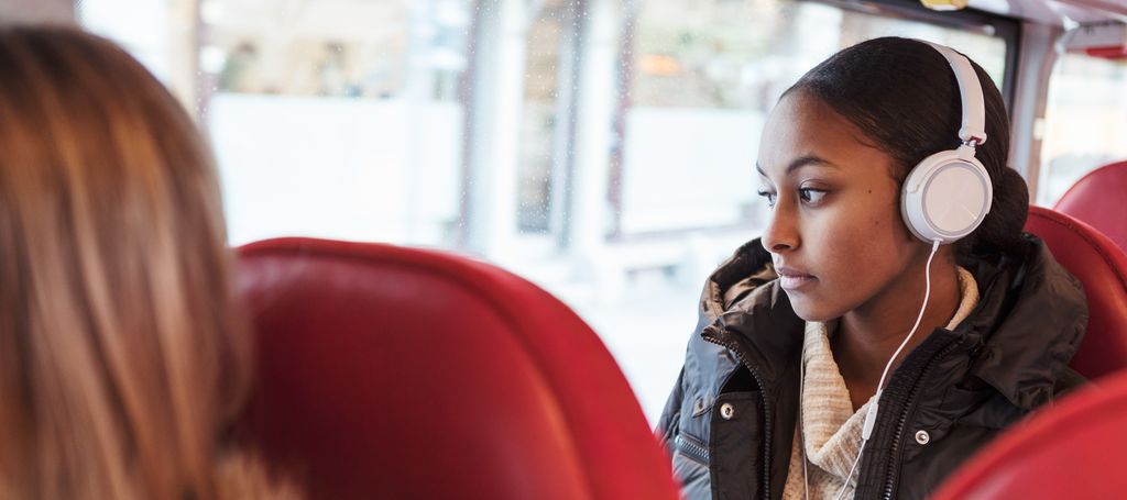 Ung jente med høretelefoner på bussen. Foto.