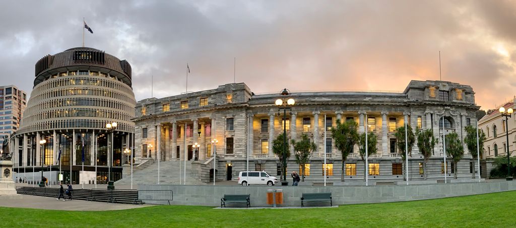 Photo: We see several buildings. To the right we see a modern building 'the Beehive' which houses the executive branch in New Zealand. To the right of it we see the parliament building, which is a Victorian style stone building.