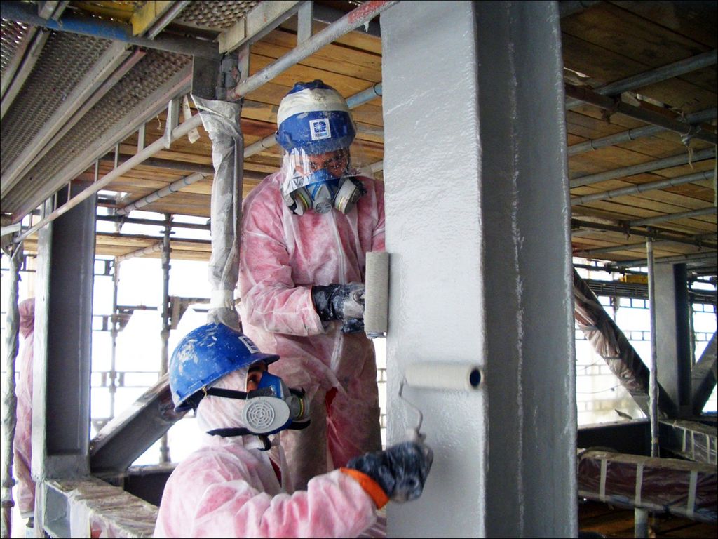 To personer med verneutstyr maler med rulle på en stålkonstruksjon. Foto.