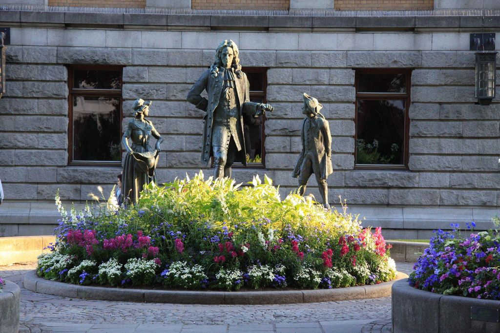 En bronsestatue av dikteren Ludvig Holberg foran Nationaltheatret i Oslo. Sammen med Holberg står to mindre bronsestatuer, alle kledd i 1700-tallsklær. Foto. 