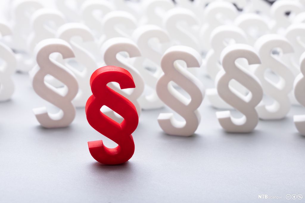 Rødt paragraftegn i forkant av mange hvite som står på rekke og rad bak det røde tegnet. Foto.