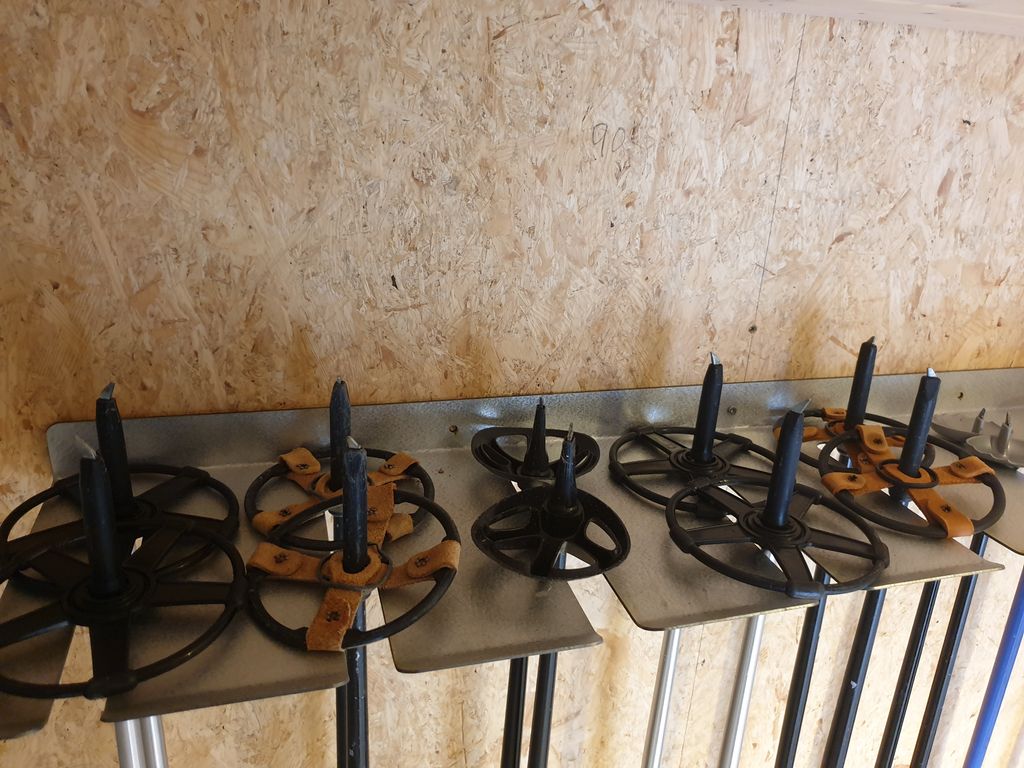 Skistavholder av aluminium. Ti par skistaver henger opp-ned på stativet. Foto.