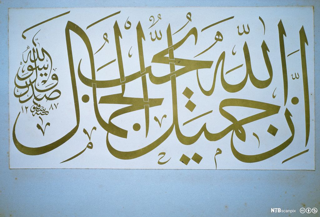 Arabisk skrift i gullfarge på hvit plakat. Foto.