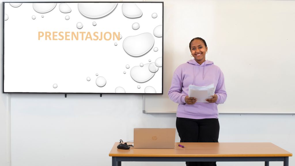Elev med notater i hendene står foran ei smarttavle der det står "Presentasjon". Foto.