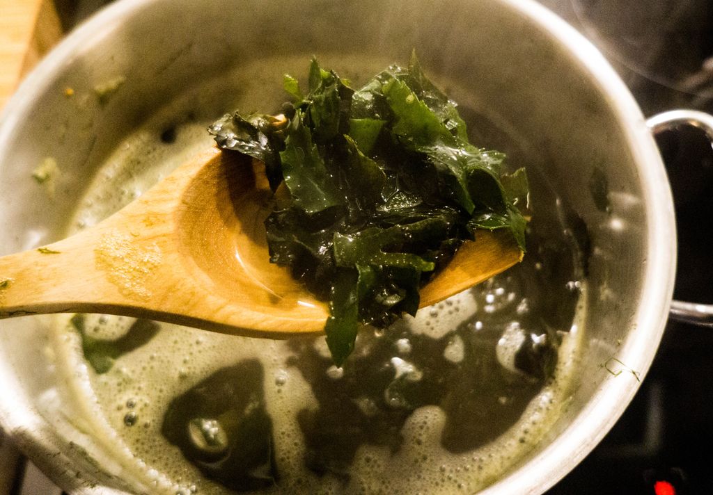 Grønn tare ligger på tresleiv over dampende gryte. Foto.