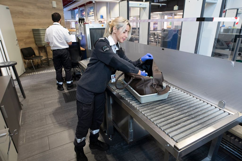 Vekter kontrollerer håndbagasje manuelt i sikkerhetskontrollen på en flyplass. Foto.