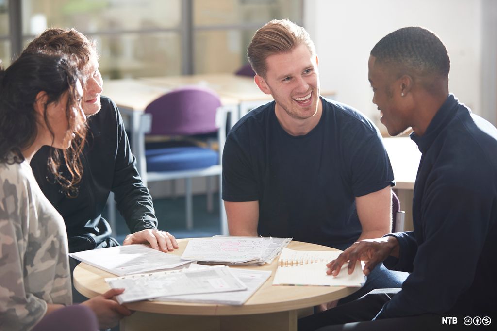 Glade ungdommer snakker sammen ved et bord i et bibliotek. Foto.