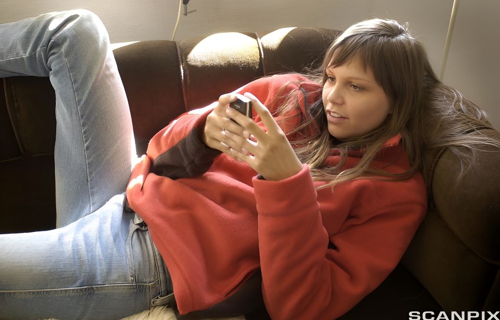 Ung jente med mobiltelefon sender SMS. Foto.