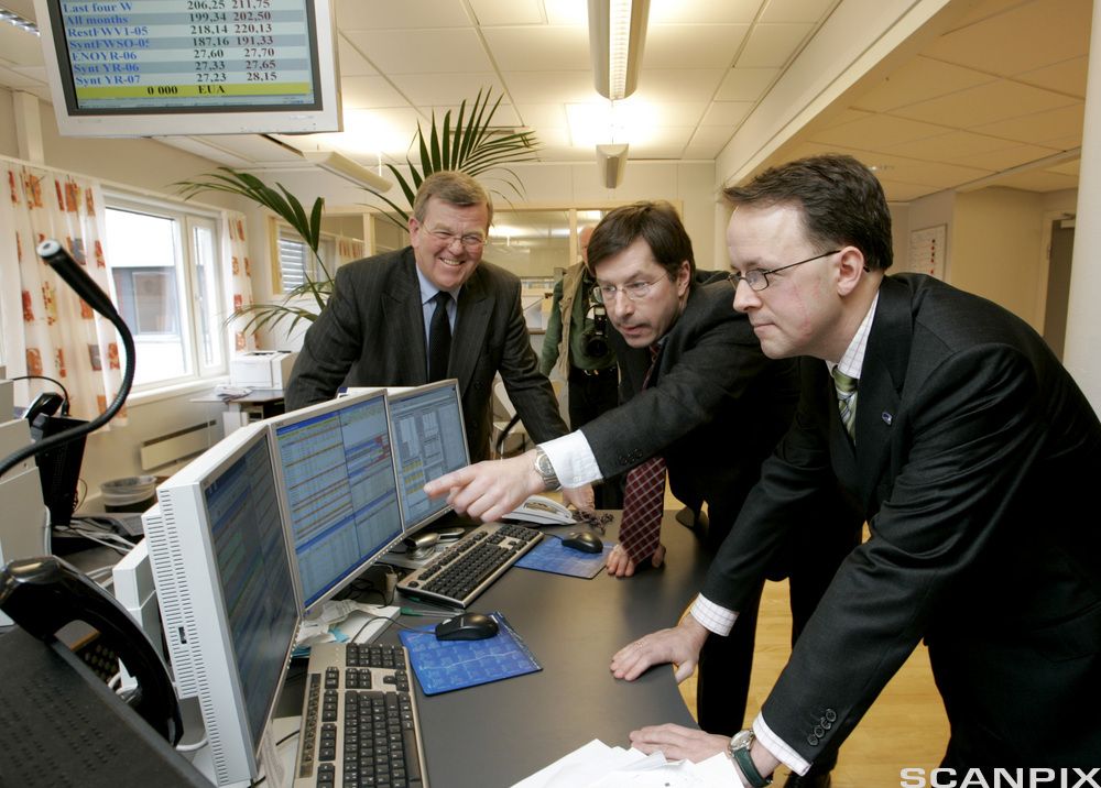 Tre personer står ved dataskjermer.