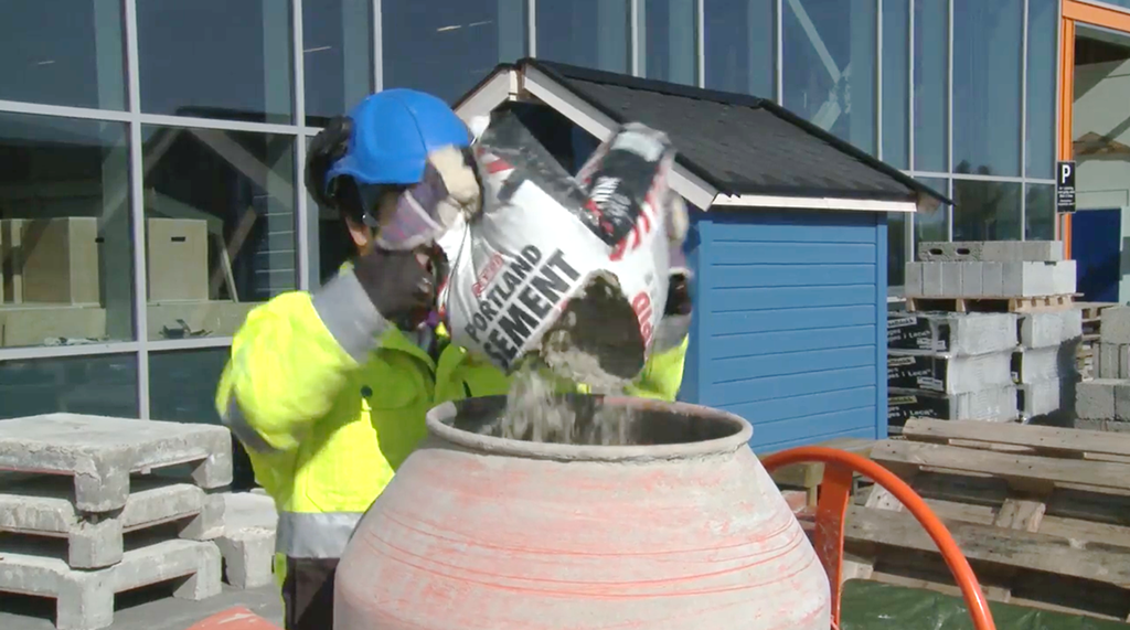 Arbeider som tilsetter sement i en mørtelblander. Foto.