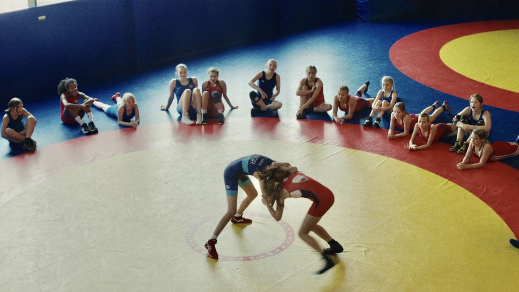To personer i en bryteposisjon med unge jenter som sitter i en ring på gulvet og ser på. Foto.