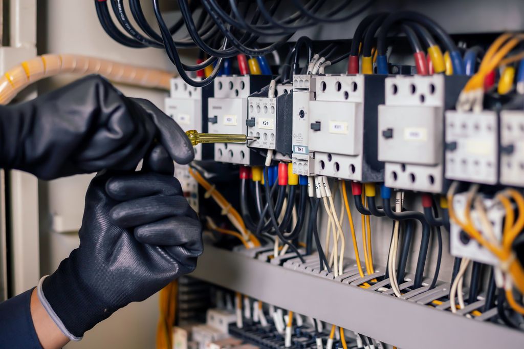 To hender med isolerhansker skrur på komponenter i et elektrisk skap. Foto.