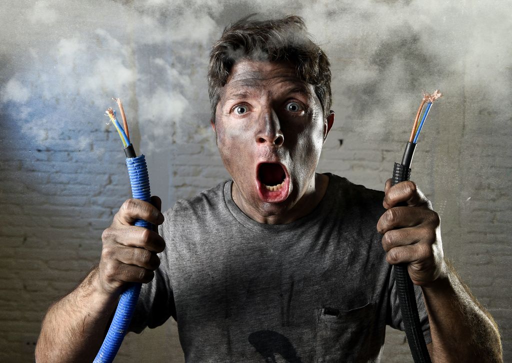 Mann som har kortslutta en elektrisk kabel. Ansiktet hans er fullt av sot, og han ser sjokkert ut. Foto.