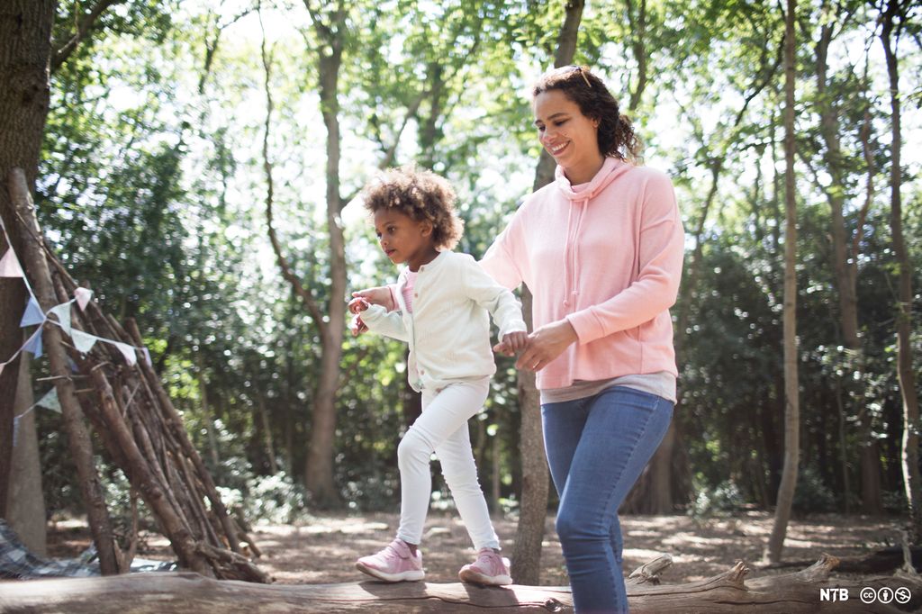 En voksen hjelper ei jente med å balansere på en stokk. Foto.