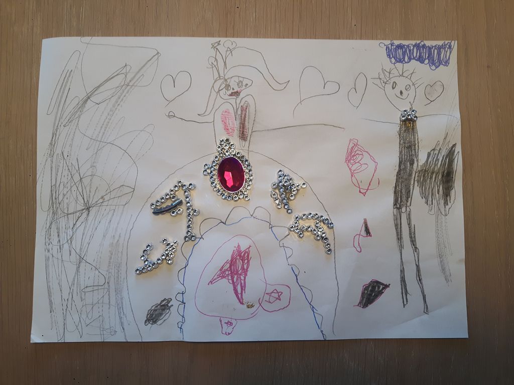 En knust plast-tiara med mange små diamanter og en stor rosa diamant er limt på ei tegning av et brudepar. Bruden har glitrende biter på skjørtet sitt og brudgommen har en liten bit av tiaraen som sløyfe. Foto.