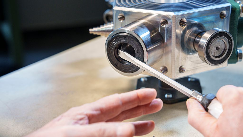 Mekanisk del der ei hånd presser et skrujern mot en svart gummiring. Foto.