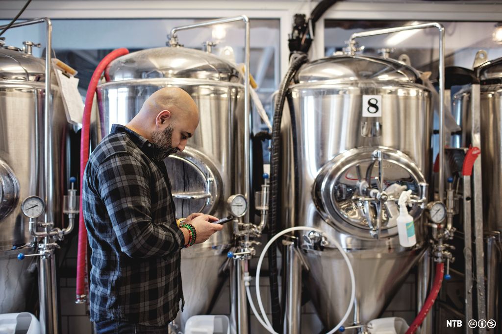 En mann trykker på mobilen i et ølbryggeri. Foto.